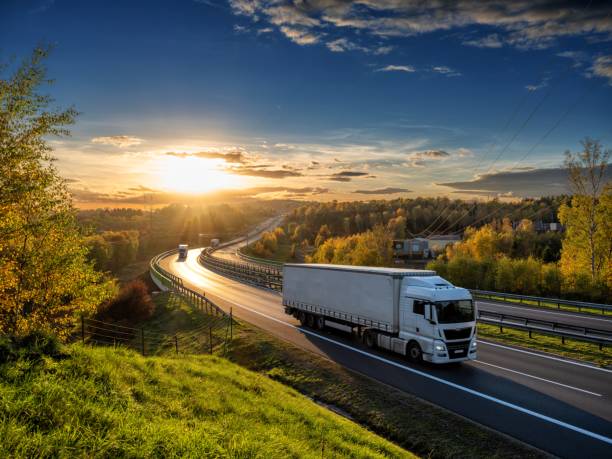 White trucks driving on the highway winding through forested landscape in autumn colors at sunset White trucks driving on the highway winding through forested landscape in autumn colors at sunset delivery van stock pictures, royalty-free photos & images