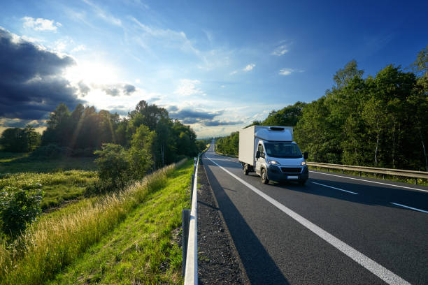 Delivery car on the road in a landscape at sunset Delivery car driving on the asphalt road between a forest in a rural landscape at sunset delivery van stock pictures, royalty-free photos & images