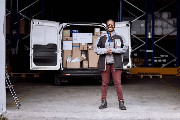 Delivery woman standing in front of a loaded van and smiling and looking at camera Young woman wearing winter delivery uniform looking at camera and standing in front of a delivery van delivery van in depot stock pictures, royalty-free photos & images